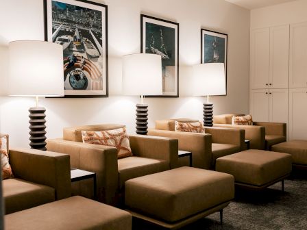 A modern waiting room with tan chairs, matching ottomans, tall stacked lamps, framed wall art, and a white-paneled closet in the back.