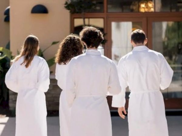 Four medical staff in white coats walk toward a building entrance labeled &ldquo;Ocean&hellip;&rdquo; on a sunny day, backs to camera.